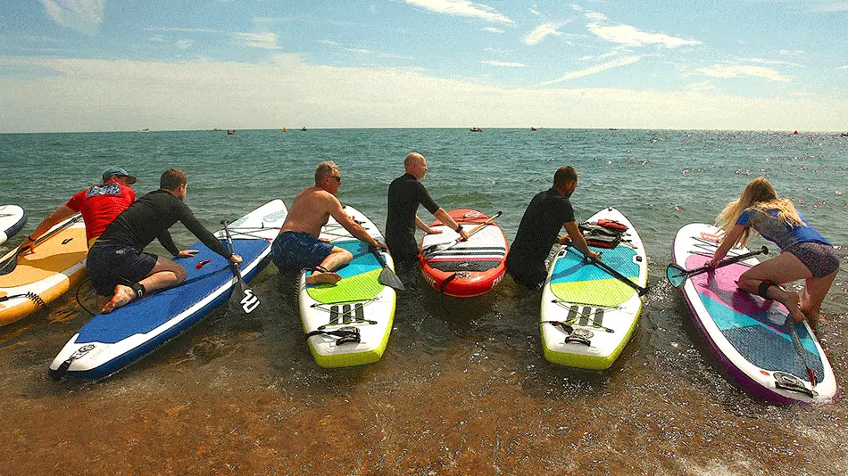 Group of men starting paddle boards on beach